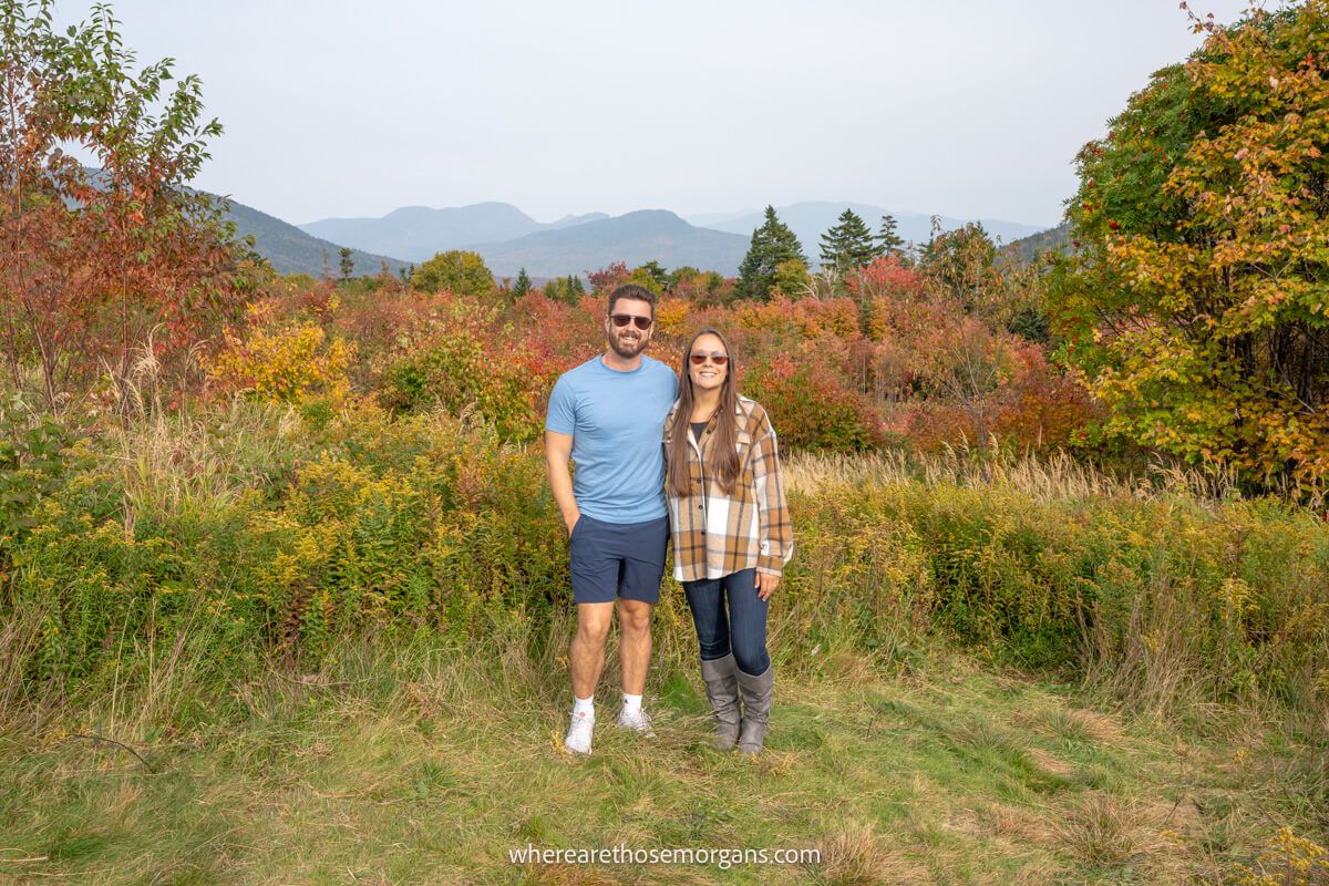 Couple standing together on grass with colorful leaves and distant views over rolling mountains