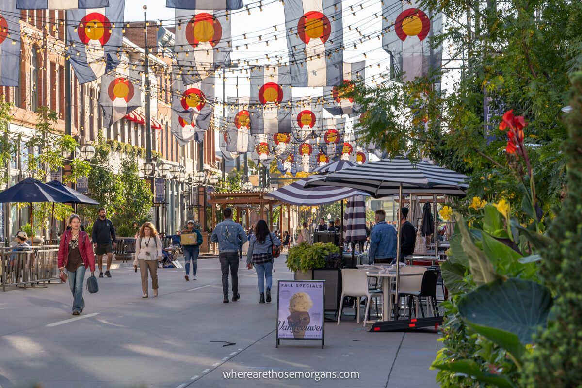 Pedestrians walking through a paved area with restaurants and bars to each side, and hanging flags with fairy lights