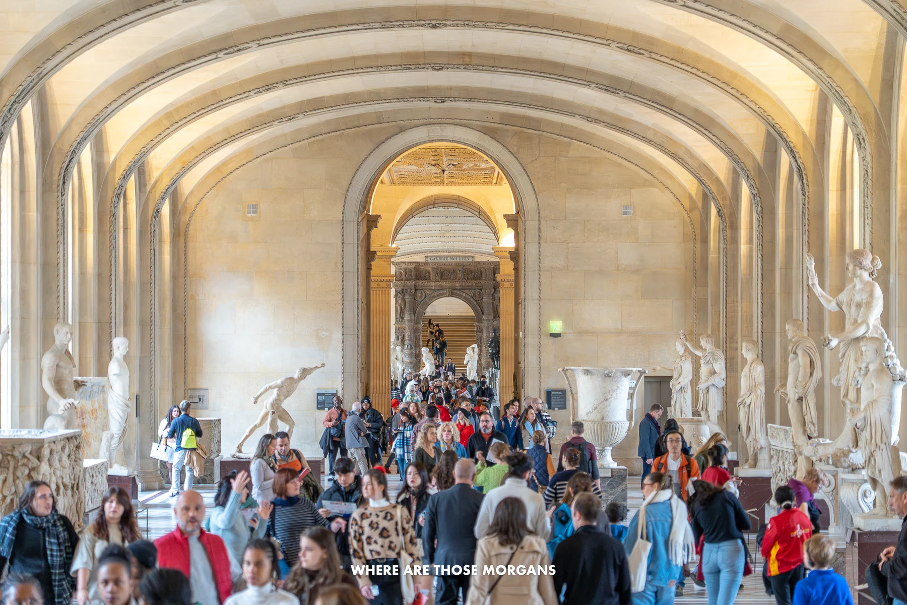 Photo of crowds of tourists walking through a wide open marble hall at the Louvre museum