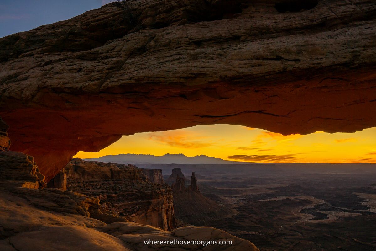 Photo of Mesa Arch in Canyonlands before sunrise with deep yellows in the sky beginning and the valley below covered in shadow