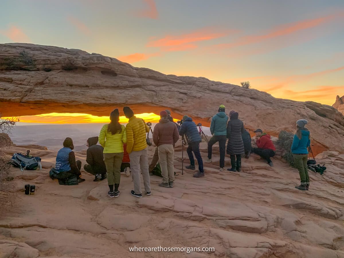 Lots of people with cameras and phones taking images of a natural rock formation at dawn