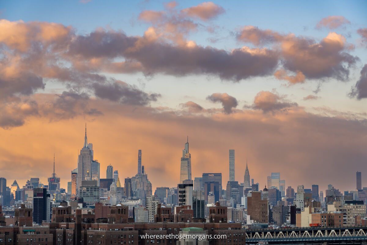 Photo of the Midtown Manhattan skyline from far away under a colorful sky with clouds