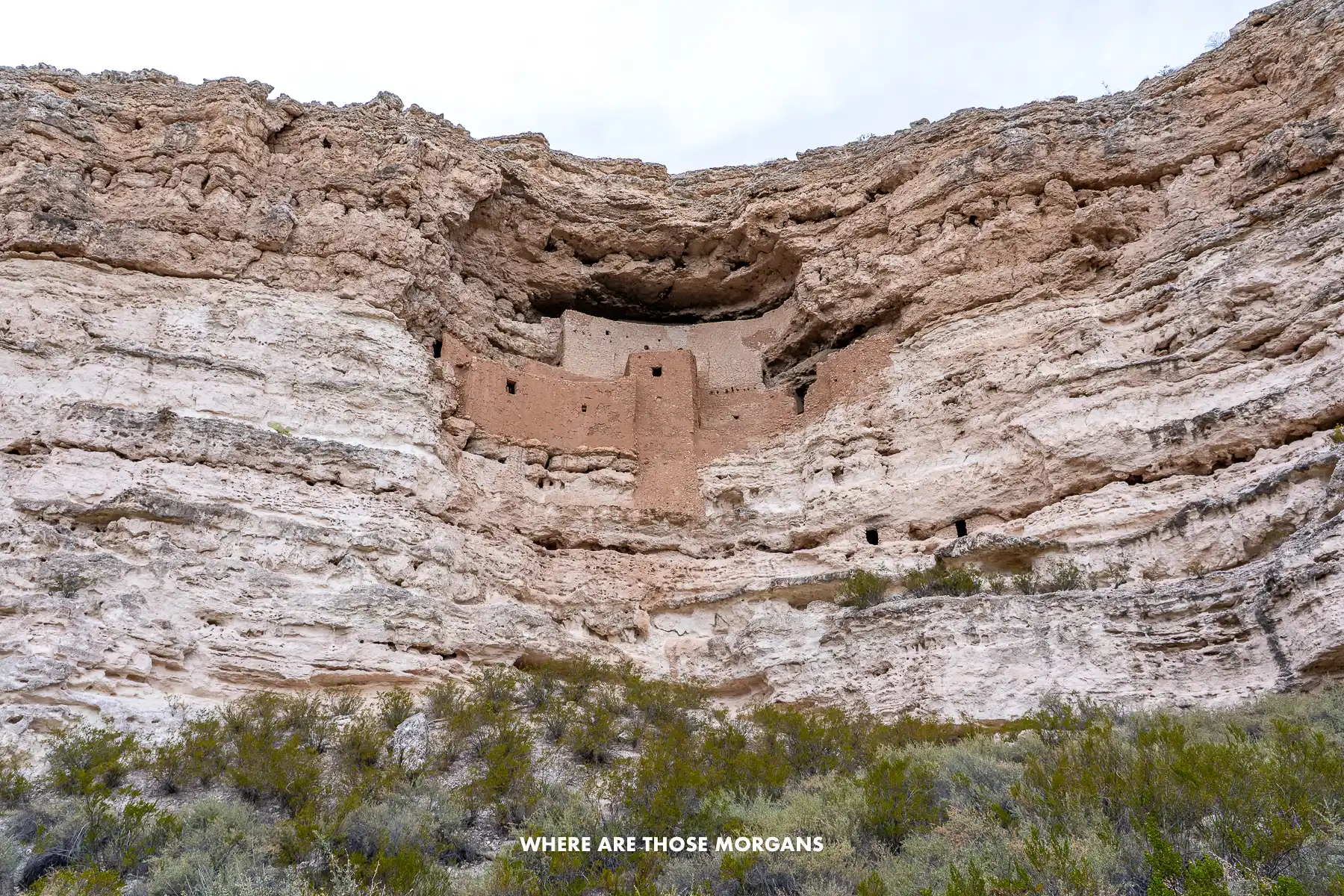Looking up at a huge cliff with a well preserved ancient dwelling high up