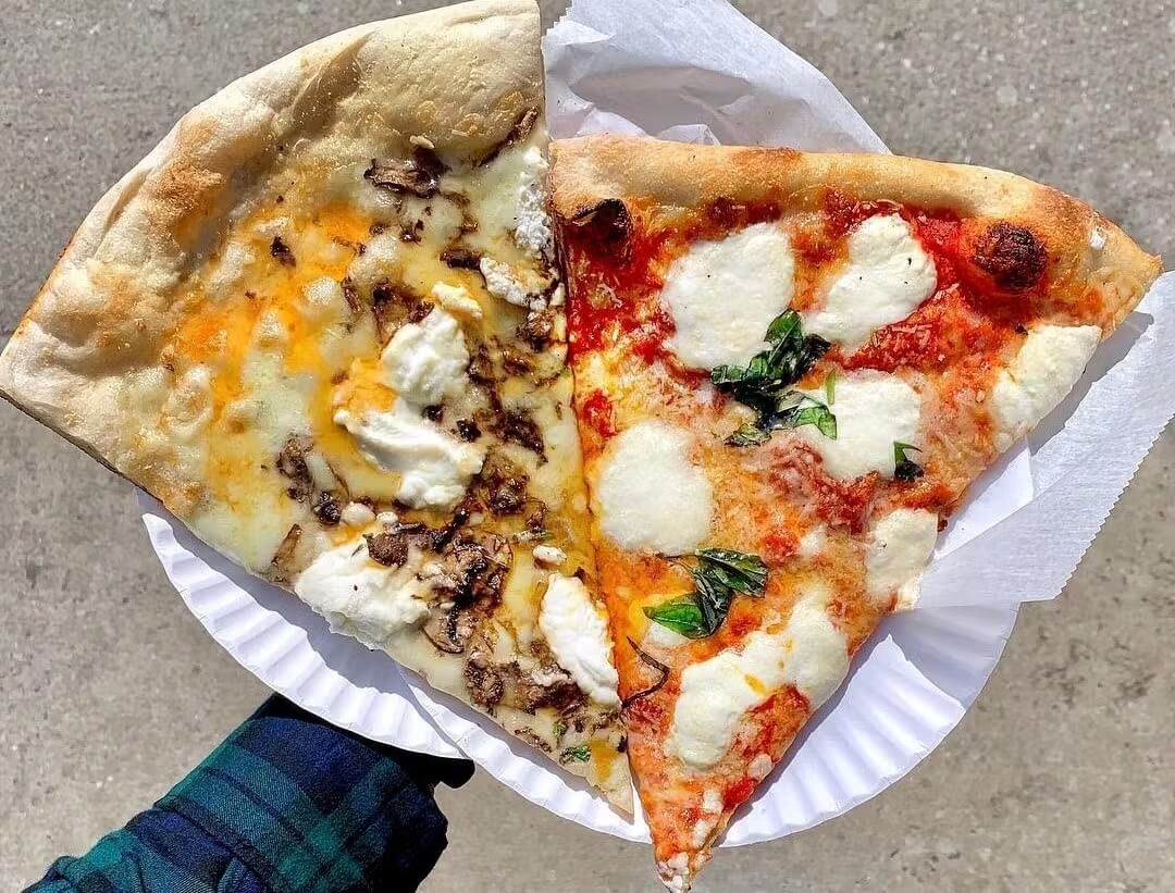 Photo of an arm holding two paper plates with slices of pizza