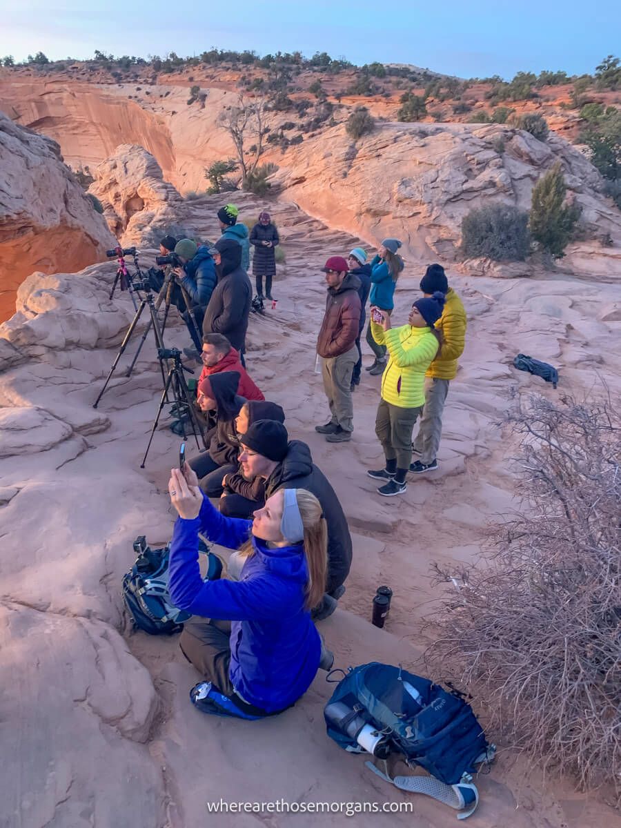 Line of photographers with cameras and tripods crouched or stood on a rocky surface looking at the sun rising