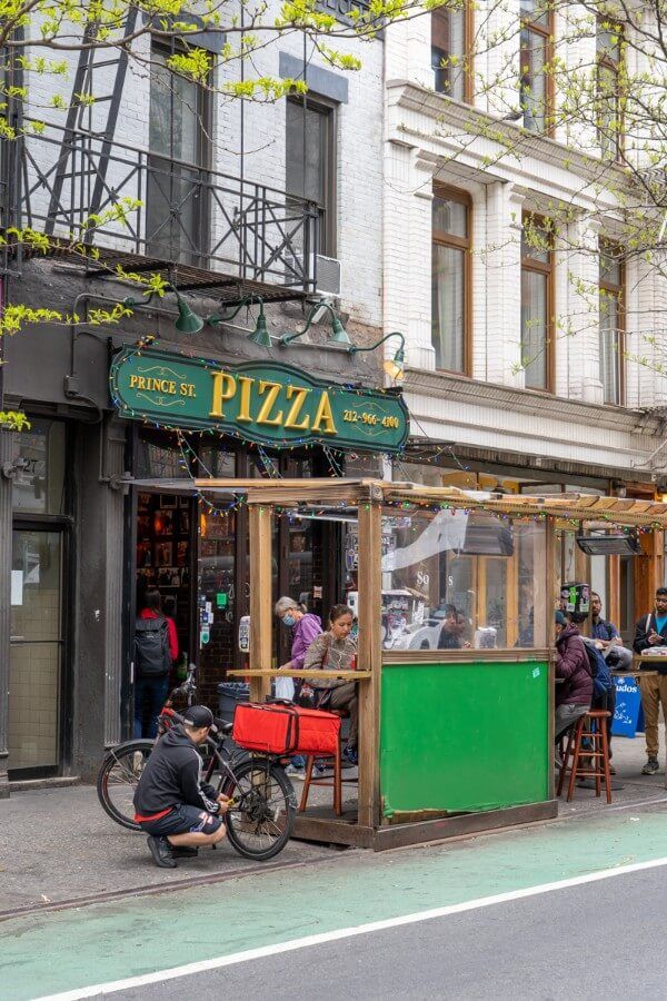 Photo of the exterior of a food establishment with outdoor seating in a row of buildings on a roadside