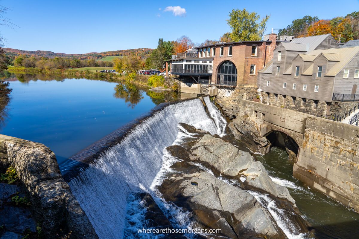 Waterfall with rocks and still water backed by houses and a restaurant with balcony