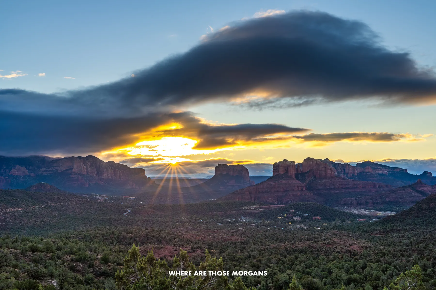 Wide open view of Sedona's red rock landscape at sunrise with the sun bursting through clouds