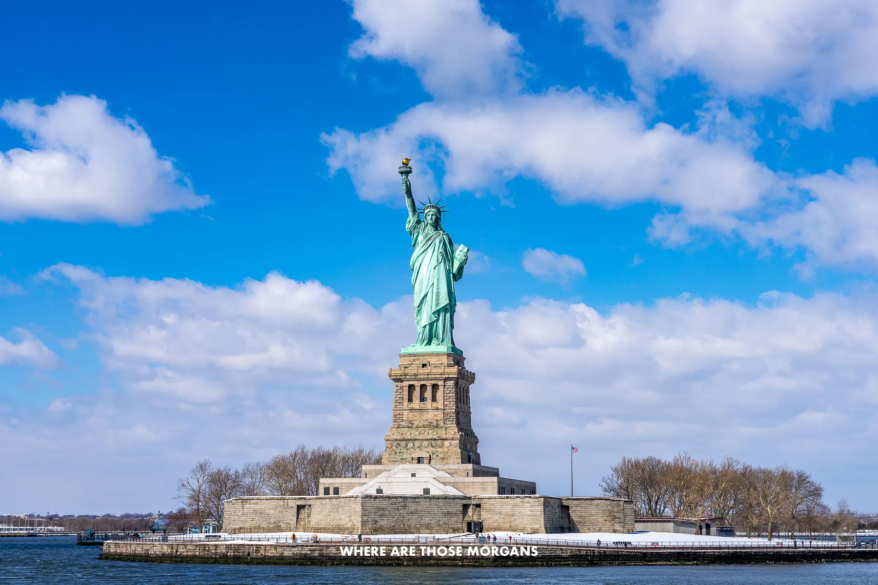 Front-on photo of the Statue of Liberty on Liberty Island under a blue sky with light clouds
