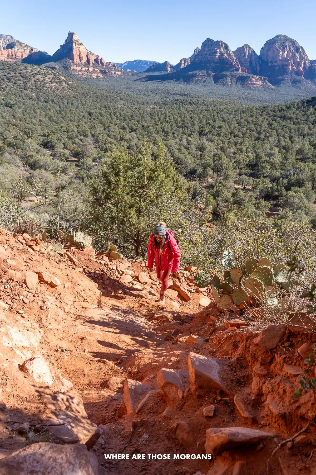 Kristen from Where Are Those Morgans climbing a steep rocky path to Sedona's Birthing Cave with far reaching views behind