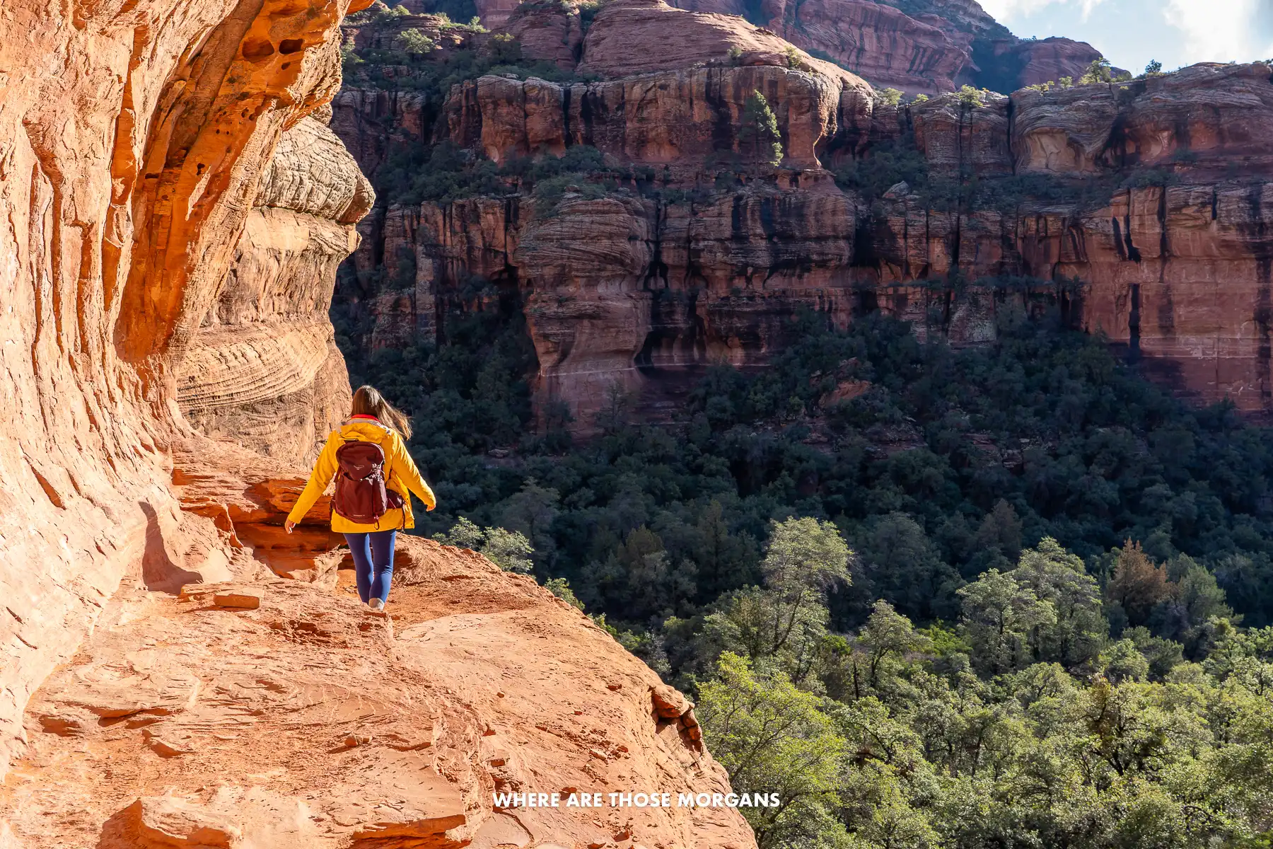 Kristen from Where Are Those Morgans walking across a narrow red rock shelf with drops to vegetation below in Arizona