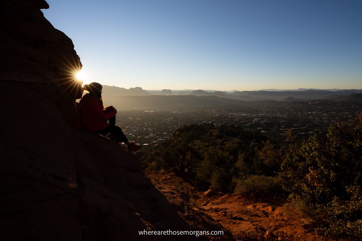 Hiker sat on red rocks enjoying serene far reaching sunrise views over Sedona's red rock landscape