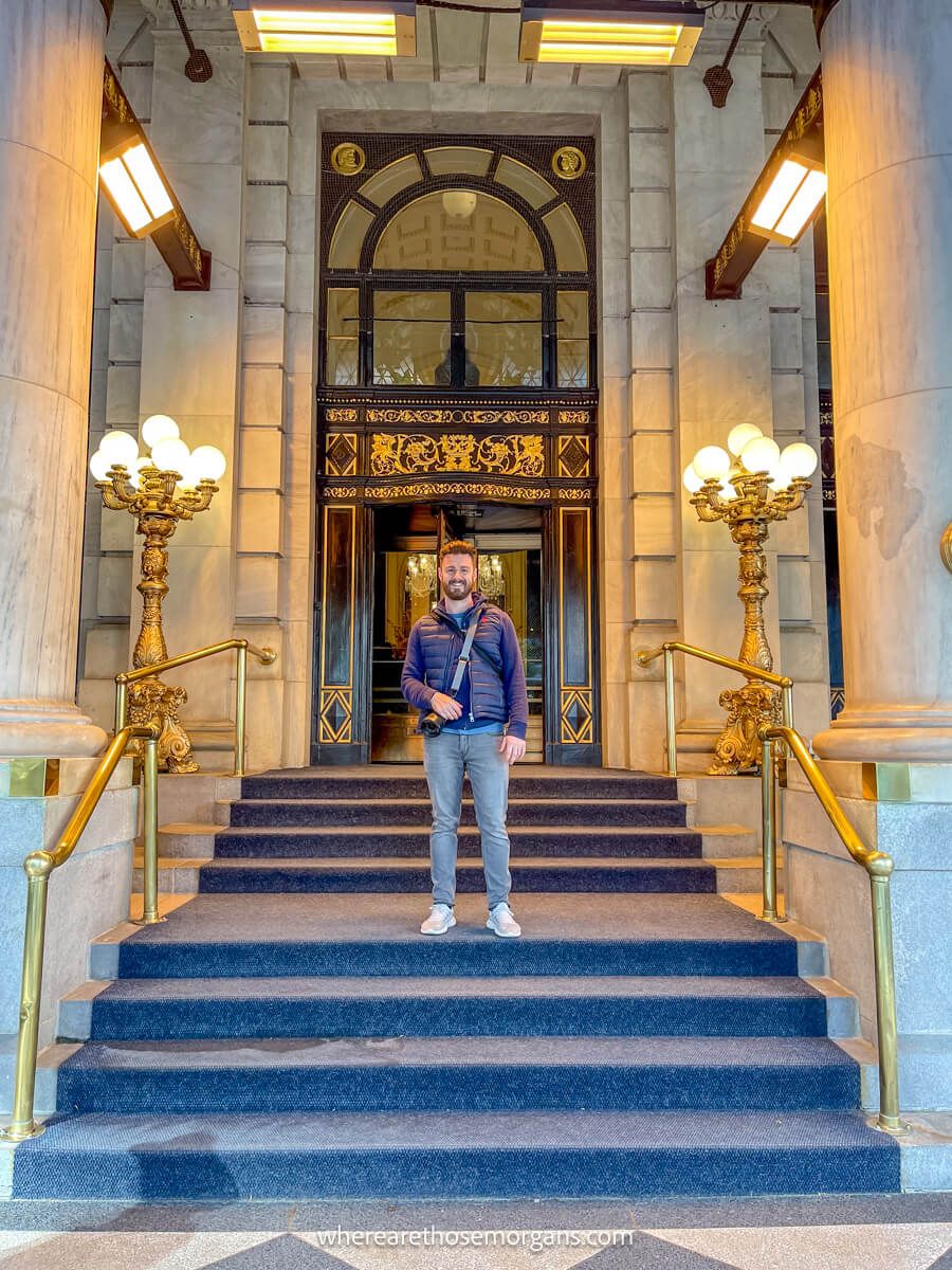 Photo of a tourist standing on a multi tier staircase at the entrance to a hotel with lots of lights behind next to the door