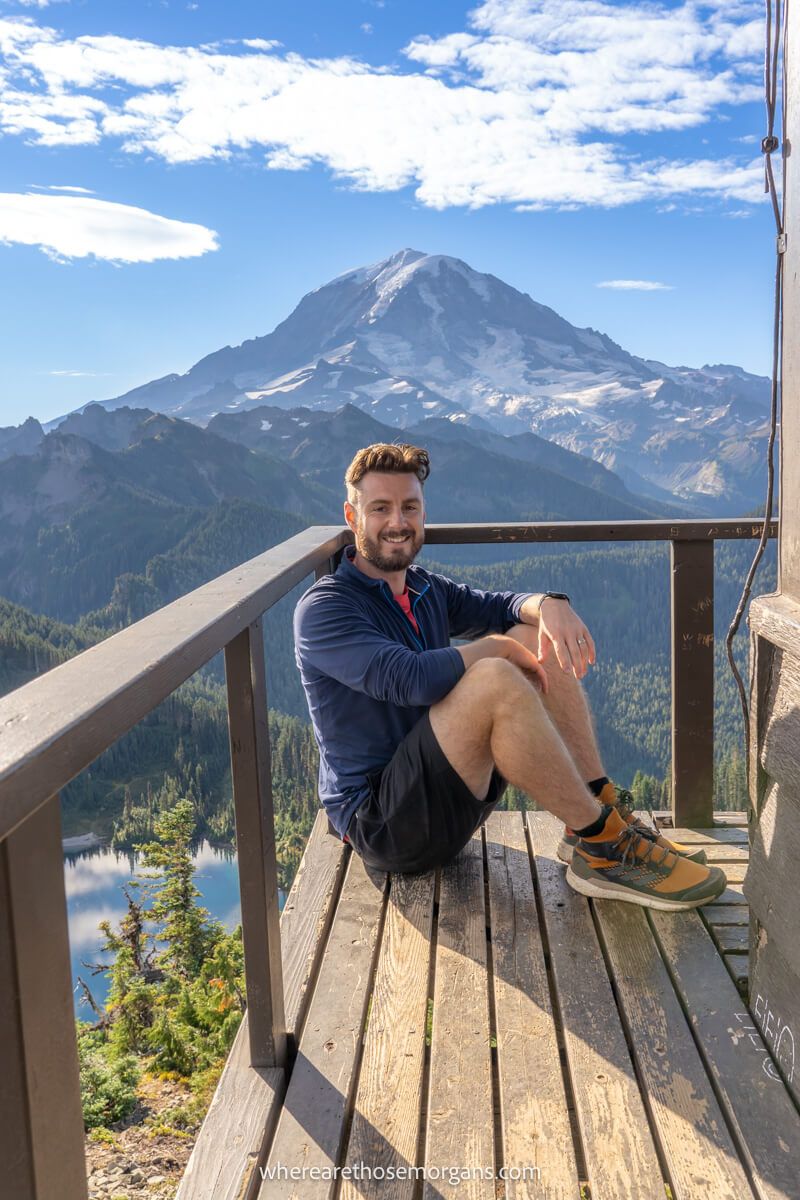 Hiker sat in the corner of a fire lookout tower with views over a volcano in the distance on a clear day