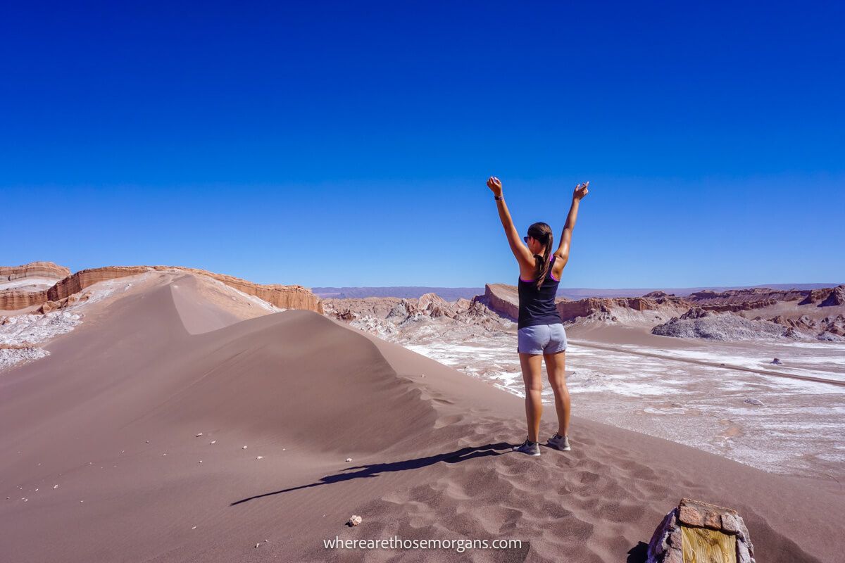 Tourist stood with arms in the air on a sand dune near San Pedro de Atacama on a sunny day with blue sky