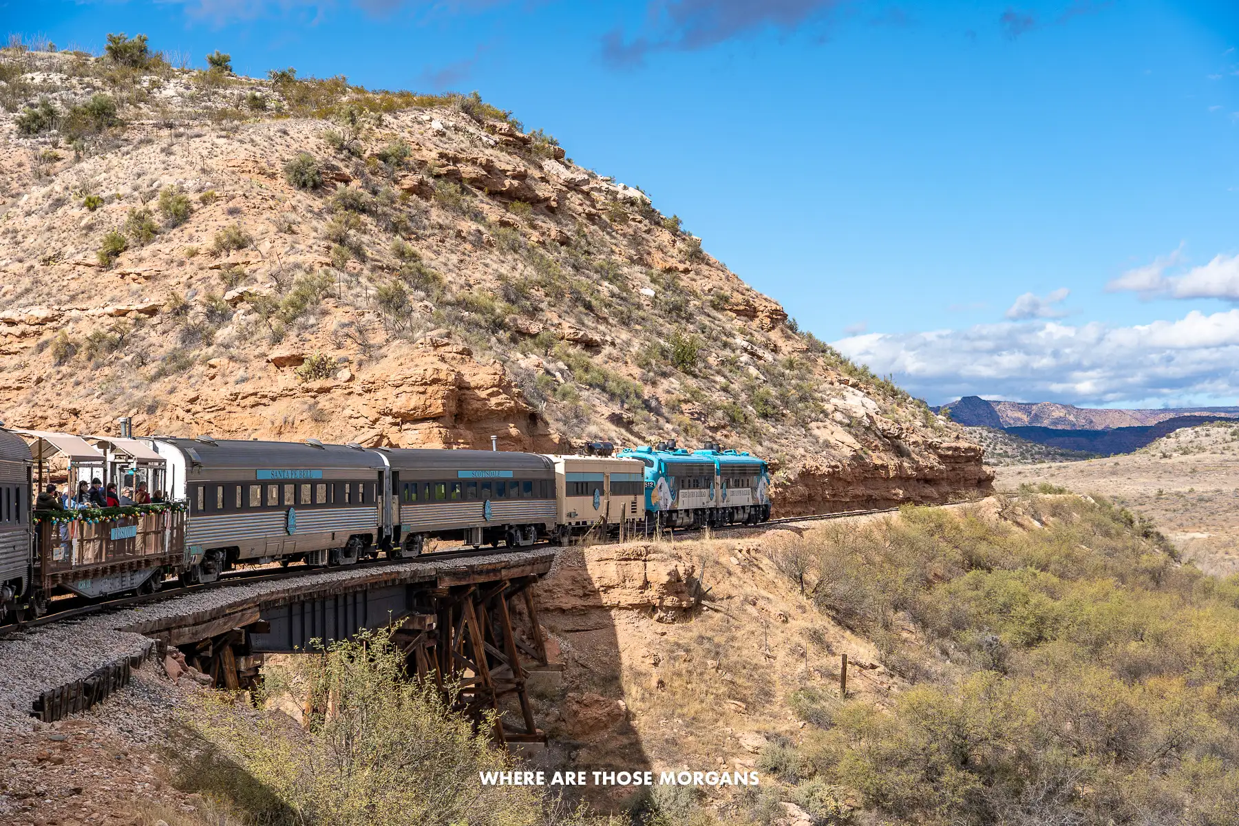 Old train curving around a red rock hill over a bridge in the desert