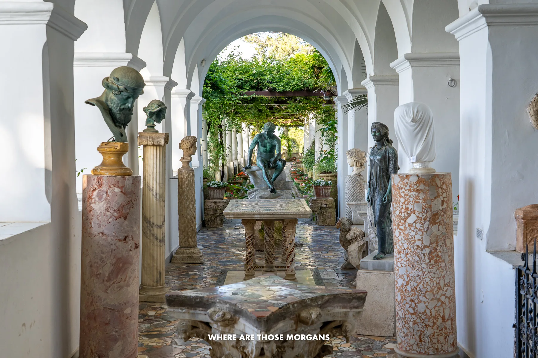 Statues and busts in an outdoor walkway with marble floor and columns in a villa in Capri