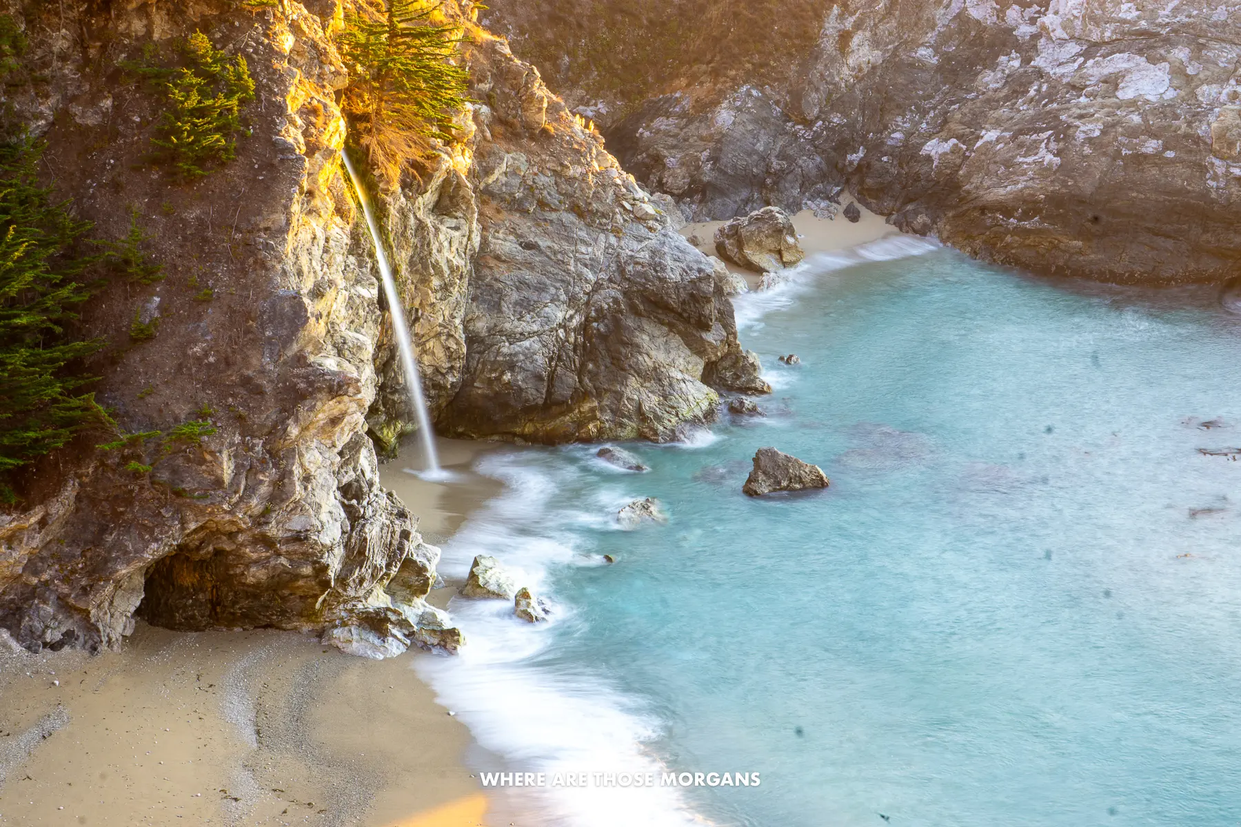 Thin waterfall dropping off a cliff edge onto a beach and the sea