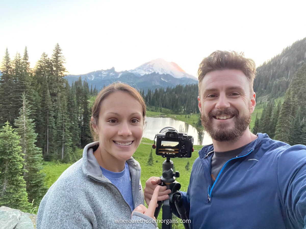 Photo of Mark and Kristen Morgan from Where Are Those Morgans taking a selfie with a camera on a small tripod and views over Mt Rainier and Tipsoo Lake on the Naches Peak Loop hike in Washington