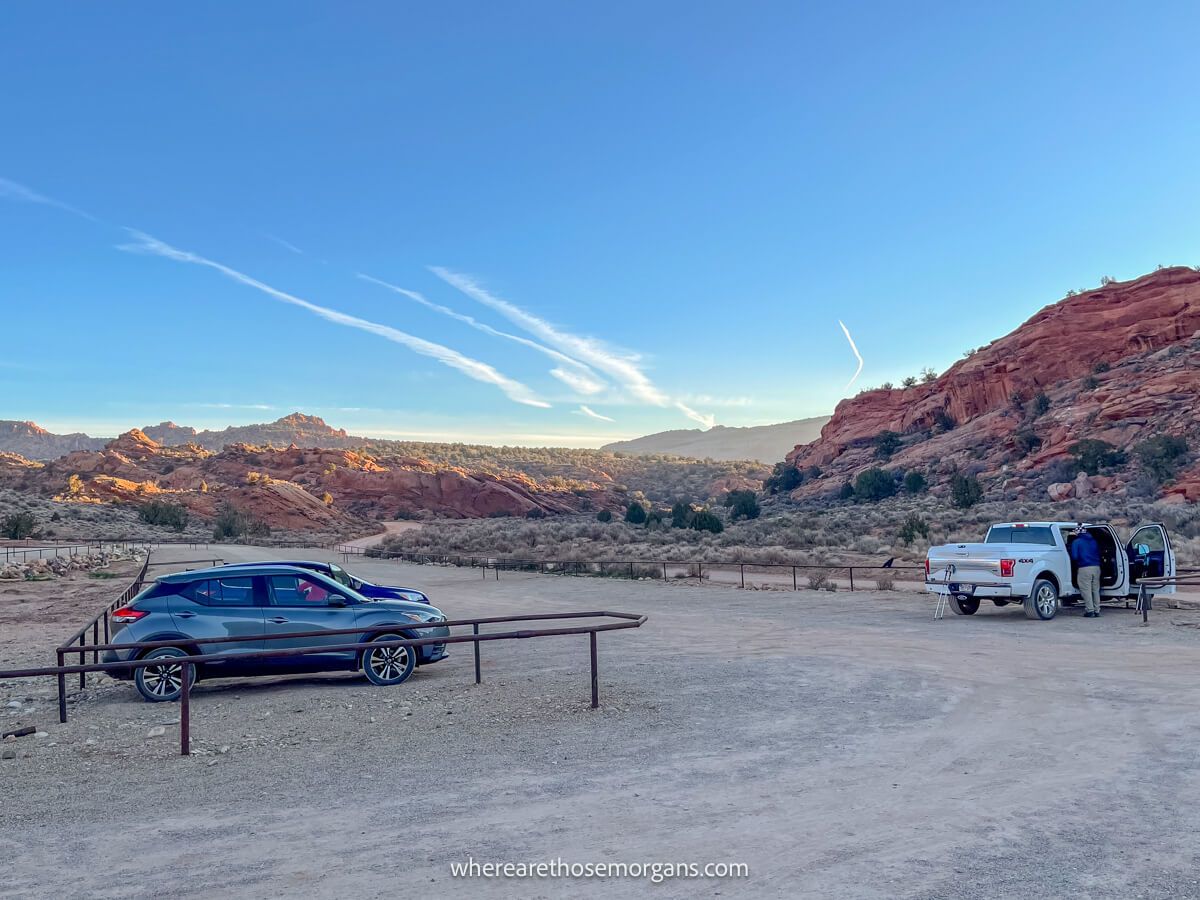 Gravel parking area with metal fences and a few cars parked surrounded by red rocks and blue sky