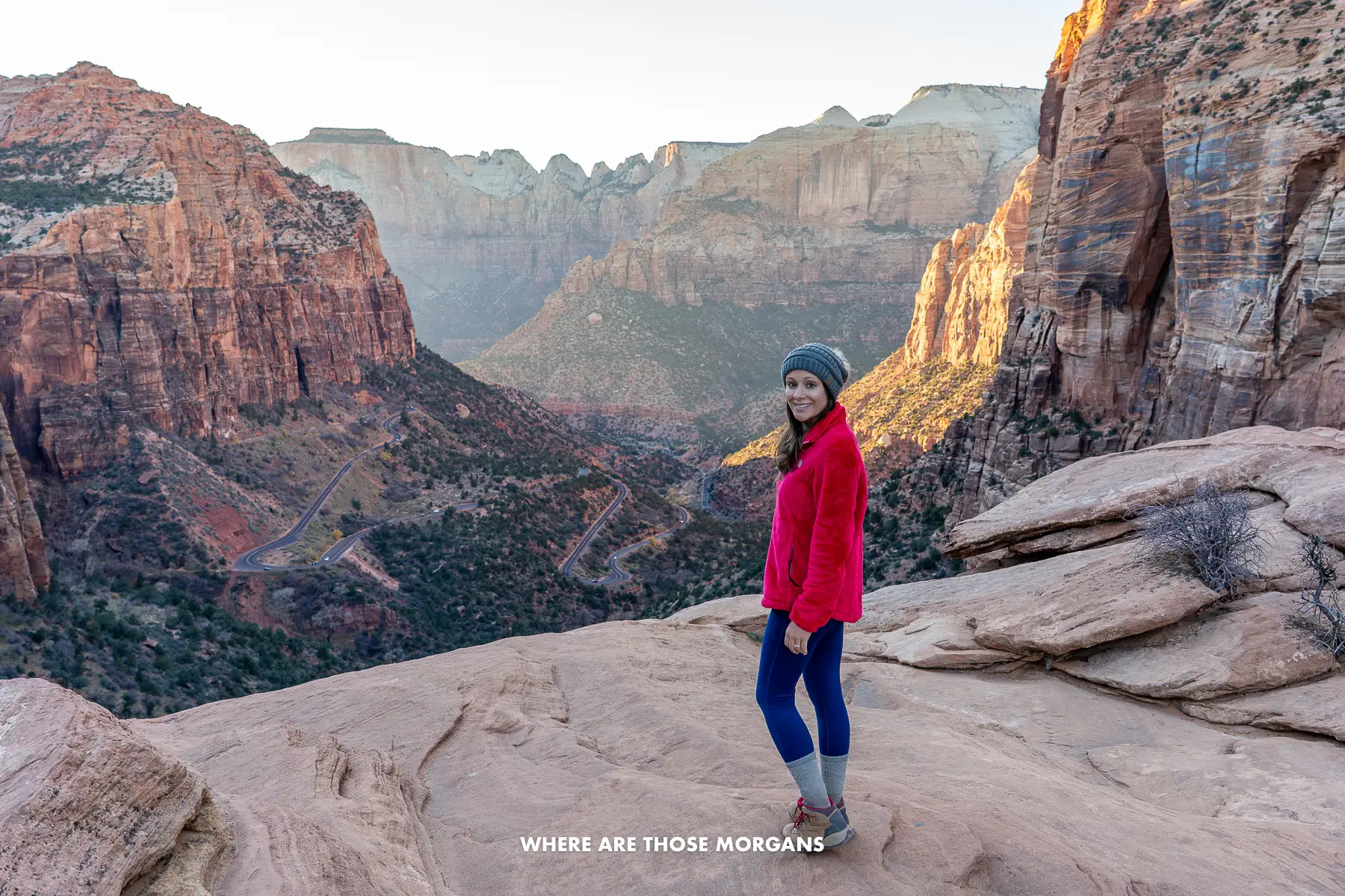 Kristen from Where Are Those Morgans standing on the edge of a red rock cliff with sunset views into a deep canyon behind