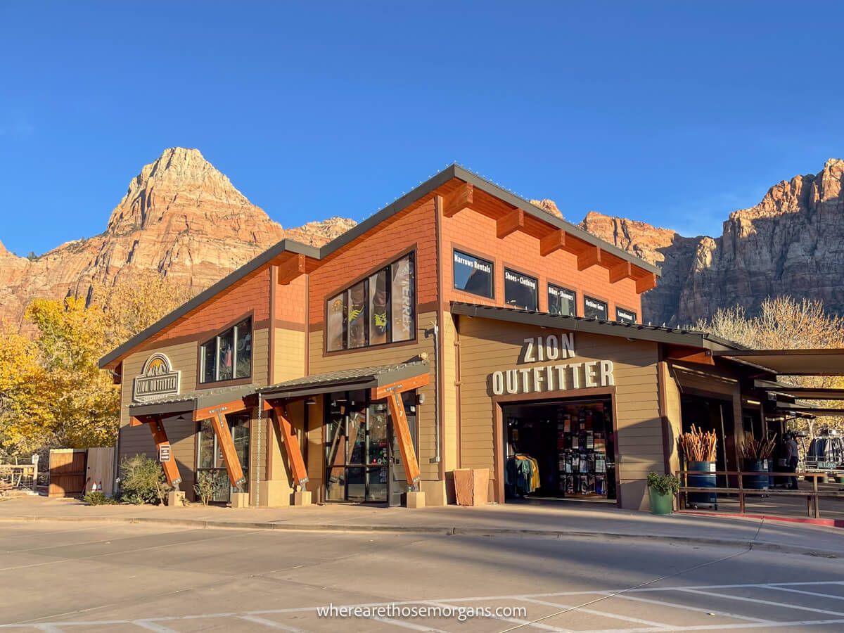 Exterior photo of Zion Outfitter building in Springdale with towering red cliffs behind and a clear blue sky