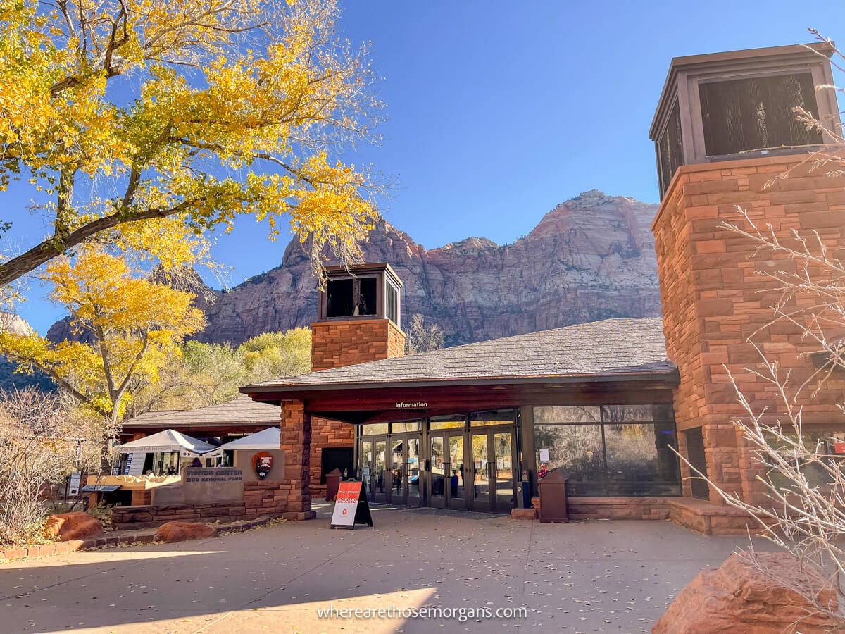 Photo of Zion visitor center from outside looking at the brick building with yellow leaves in a tree and a blue sky above